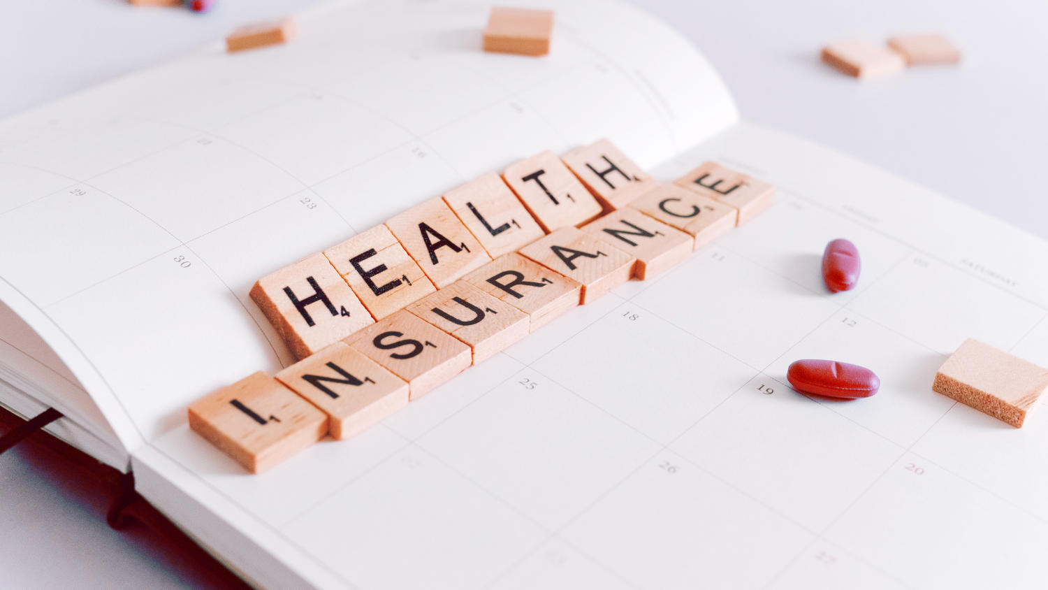 Drewniane klocki leżące na otwartym kalendarzu układające się w napis HEALTH INCURANCE, czyli ubezpieczenie zdrowotne jedyne obowiązkowe ubezpieczenie dla ZZP w Holandii.