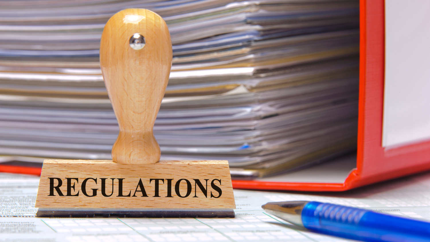 Pieczątka z napisem „REGULATIONS” na tle segregatora z dokumentami symbolizująca nowe regulacje od stycznia 2025 r. w zakresie fikcyjnego samozatrudnienia w Holandii.