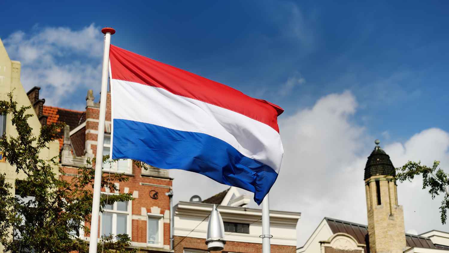 Powiewająca holenderska flaga na tle budynków, która symbolizuje niderlandzkie święto Prinsjesdag 2025, podczas którego m.in. zostały przedstawiane zmiany podatkowe w Holandii na 2026 rok.