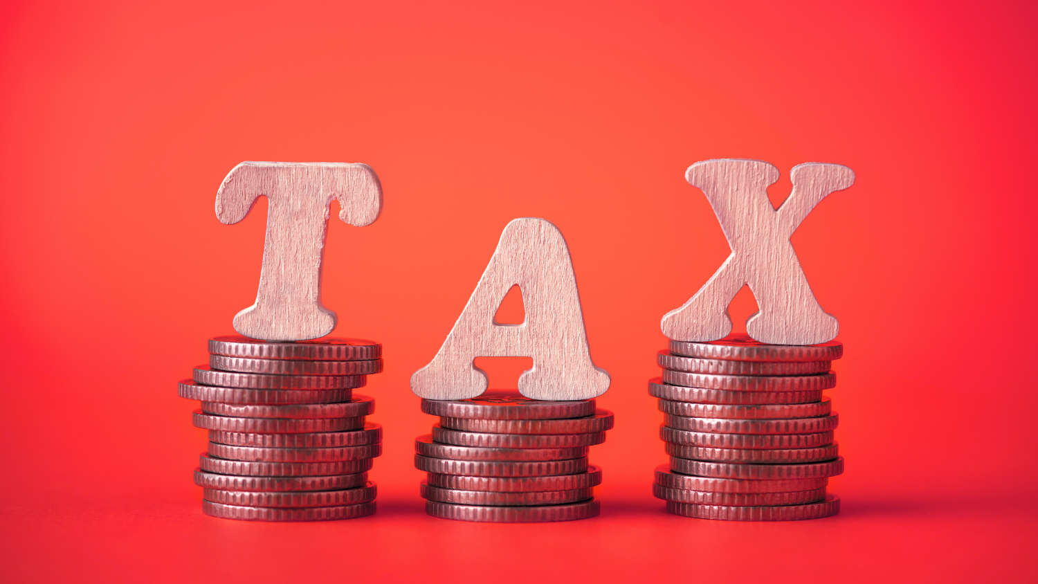 Napis TAX z drewnianych literek ustawiony na stosach monet, co oznacza zmiany podatkowe w Holandii w ulgach, progach i stawkach od 2026 r.